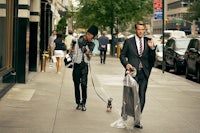 a man in a suit walking a dog on a sidewalk
