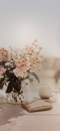 a vase of flowers on a table with a cup of coffee