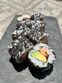 a sushi roll with avocado, salmon and sesame seeds