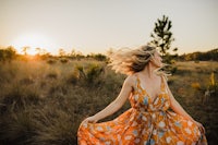 a woman in an orange floral dress is running through a field at sunset