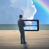 a businessman looking at a tablet computer with a rainbow in the background