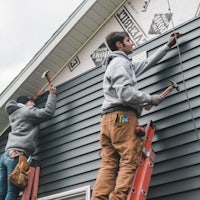 two men working on the siding of a house
