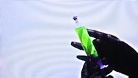 a person in black gloves holding a green syringe