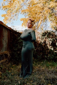a woman in a green dress posing in front of a tree