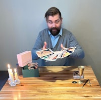 a man with a beard sitting at a table with books and candles