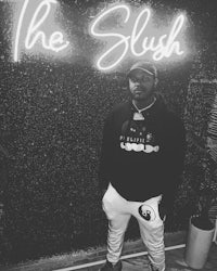 a man standing in front of a neon sign that says the slush