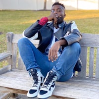 a man sitting on a bench wearing a leather jacket and sneakers