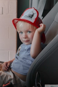 a toddler wearing a firefighter hat in a car seat