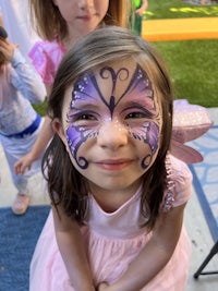 a little girl in a pink dress with a butterfly face paint