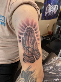 a tattoo of a praying hand on a man's arm