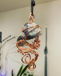 a copper wired pendant hanging from a plant
