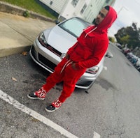 a man in a red hoodie standing next to a car