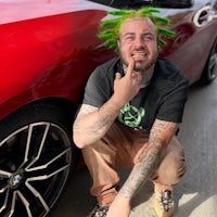 a man with green hair posing next to a red car