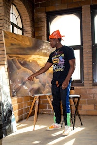 a man is pointing to a painting on a easel