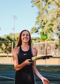 a young woman holding a tennis racket and a tennis ball
