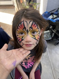 a little girl with a butterfly face painted on her face