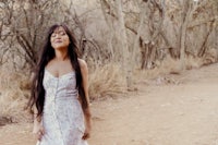 a woman in a white dress standing on a dirt road