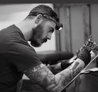 black and white photo of a tattoo artist working on a tattoo