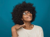 young african american woman with afro hair posing with glasses on blue background