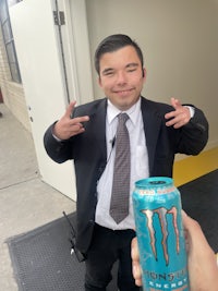 a man in a suit holding a monster energy drink