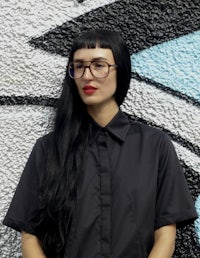 a woman wearing glasses and a black shirt in front of a graffiti wall