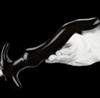 a hand holding a black plastic dildo on a black background