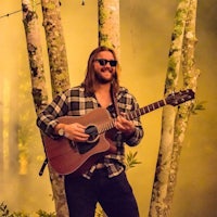 a man in sunglasses playing an acoustic guitar in a forest