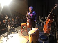 a woman standing in front of a stage with a cello and other instruments