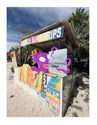 a purple octopus is sitting on the beach next to a sign that says surf trips
