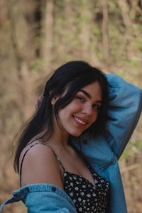 a young woman in a denim jacket posing for a photo in the woods
