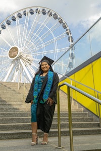 a woman in a graduation gown posing in front of a ferris wheel