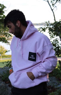 a man wearing a pink hoodie standing in front of a tree