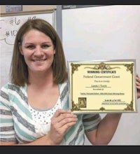 a woman holding up a certificate in front of a whiteboard