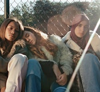three young women are sitting on a fence next to each other