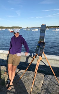 a woman standing next to an easel in front of a body of water