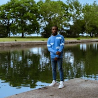 a man standing next to a body of water in a blue sweater