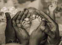 a black and white photo of hands holding a baby's feet