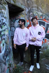 two men standing in front of a graffiti covered wall