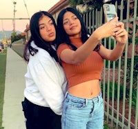 two girls taking a selfie in front of a fence