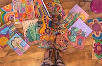a person standing in front of a pile of colorful paintings