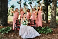 a bride and her bridesmaids pose on a bench in the woods