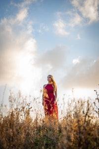 a woman in a red dress standing in tall grass