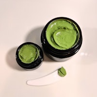 two jars of green mask on a white surface