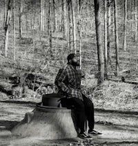 a man sitting on a stump in the woods