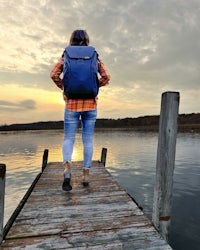 a woman with a backpack is standing on a dock at sunset