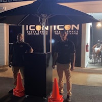 two men standing in front of an umbrella with orange cones