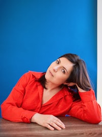 a woman in a red shirt leaning on a table