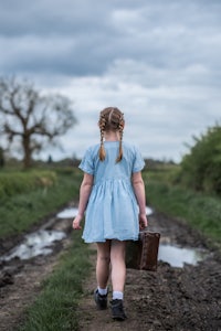 a little girl walking down a dirt road with a suitcase
