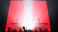silhouettes of people standing on a stage in front of a red light