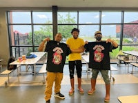 three men posing with t - shirts in a school cafeteria